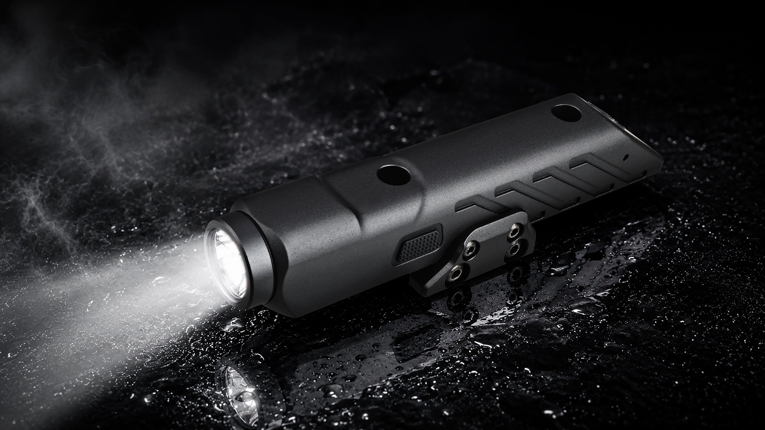 A black tactical flashlight with its front light illuminated, shown on a dark wet surface with mist in the background.