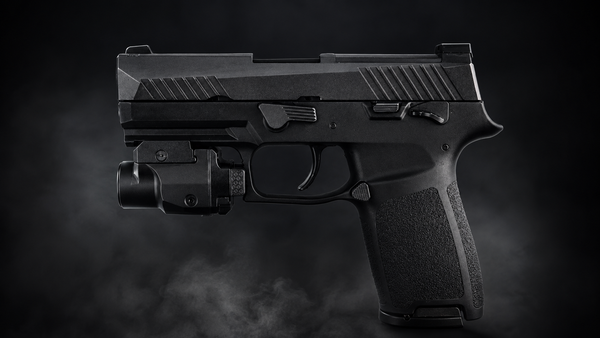 A black semi-automatic handgun with an attached black tactical light bar, shown in profile against a dark smoky background.
