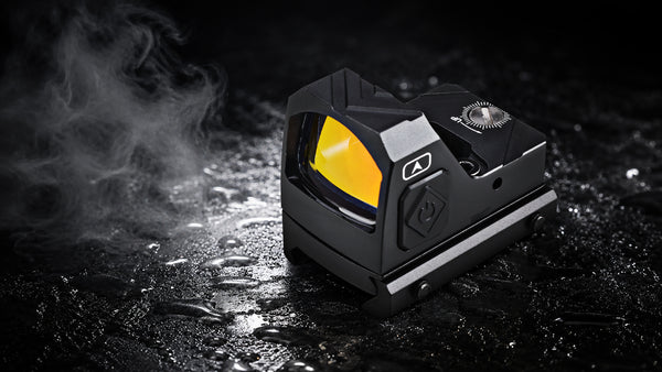 A black tactical red dot sight with a bright yellow lens, shown on a wet dark surface with steam or smoke on the left.